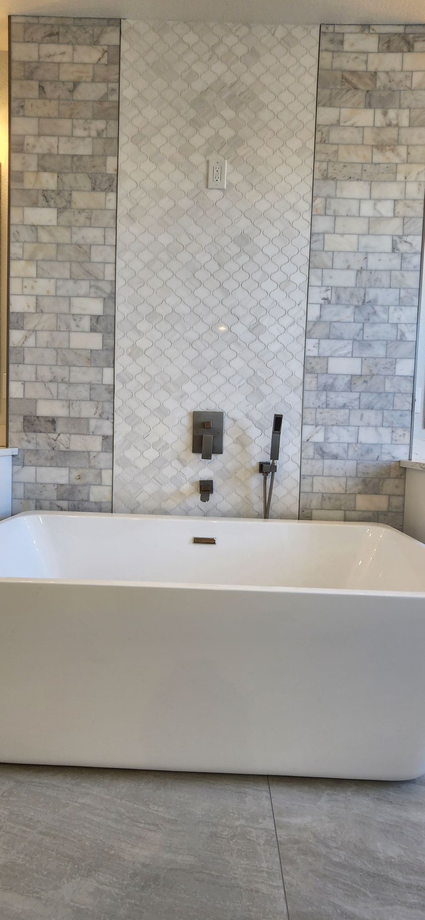 White bathtub centered in front of a tiled wall with a faucet and shower head.