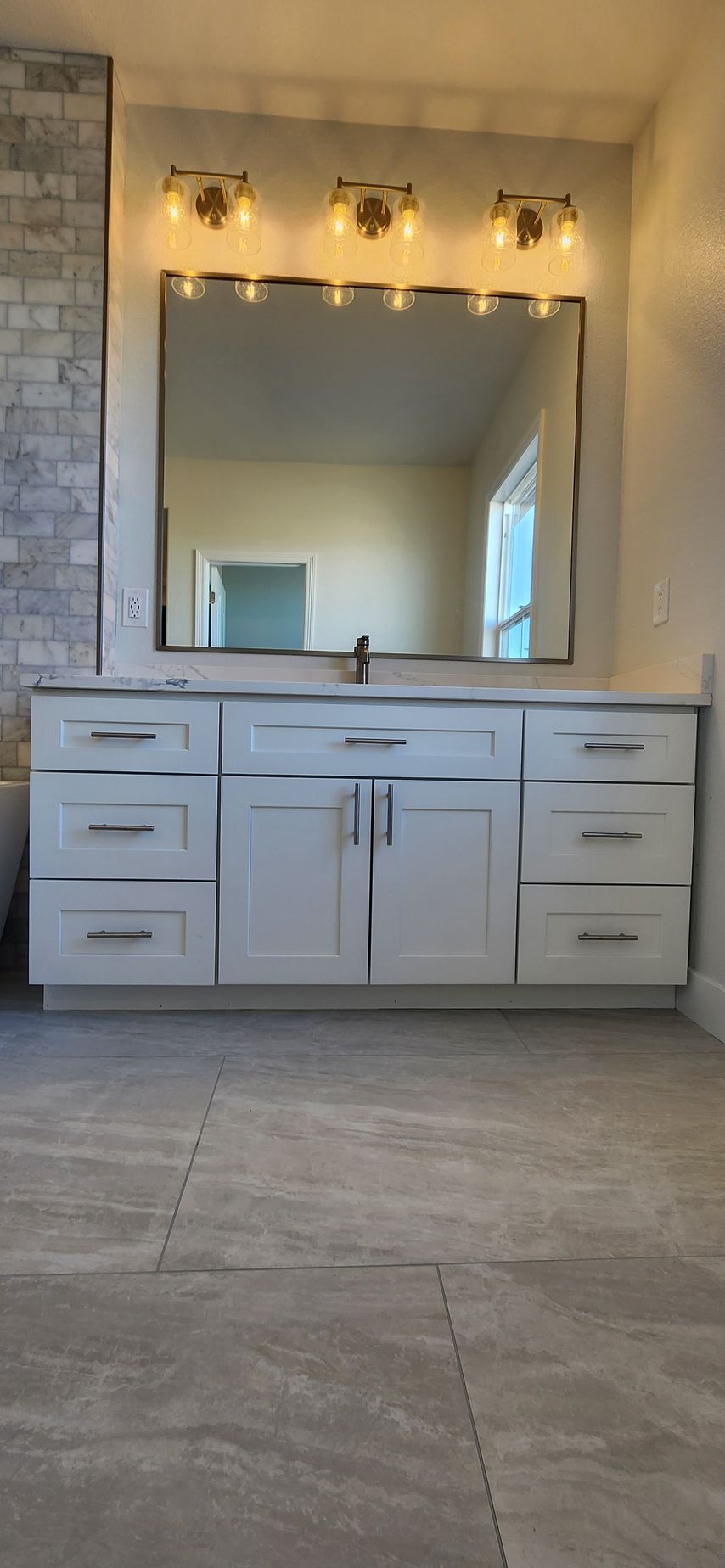 Bathroom vanity with mirror, lights, cabinets and stone tile floor.