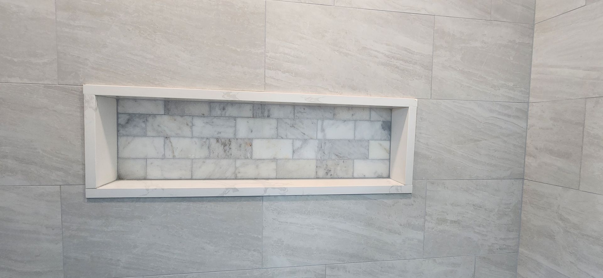 Bathroom wall with a recessed shelf lined with marble tiles.