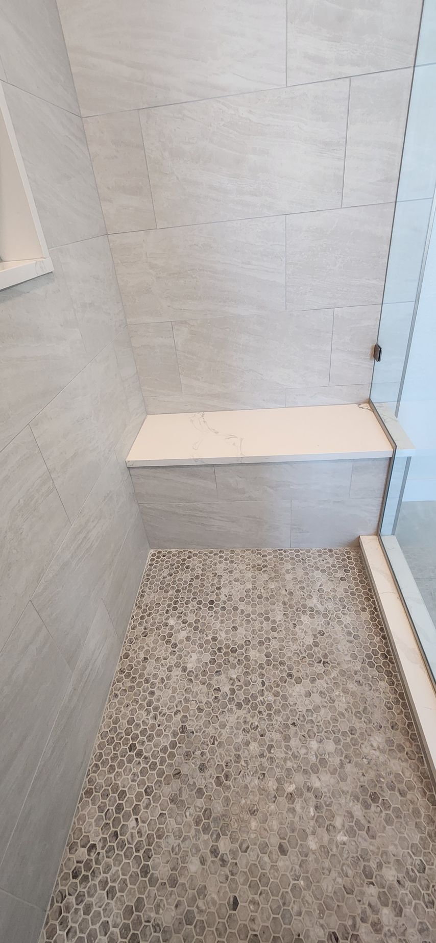 Shower with pebble floor, built-in bench, and light gray tiled walls.
