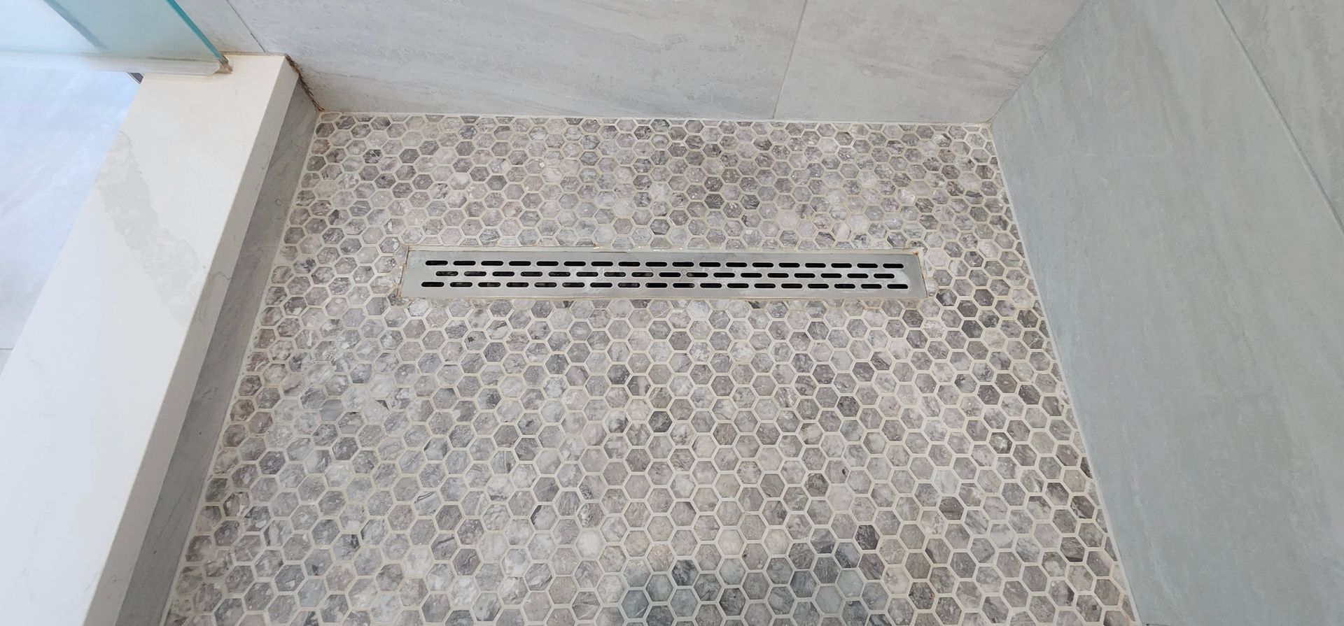 Shower floor with grey hexagonal tiles and a long, rectangular drain.