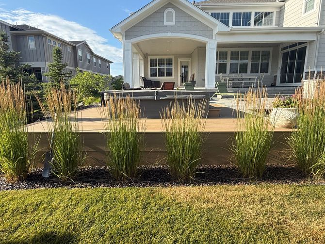 Backyard with tiered deck, tall grasses, and house with a porch in the background. Green lawn in front.