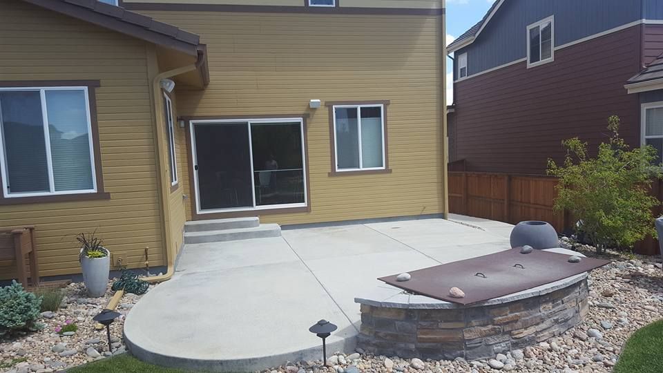 Backyard patio with a concrete surface, a fire pit, and a house with yellow siding.