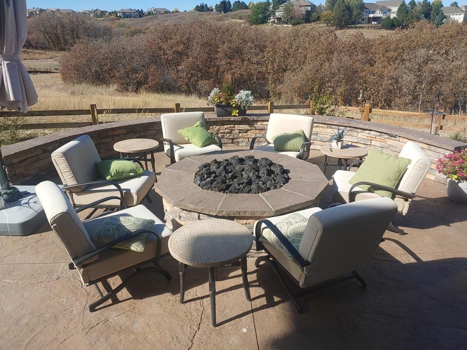Patio with a fire pit surrounded by chairs and small tables, in front of a natural landscape.