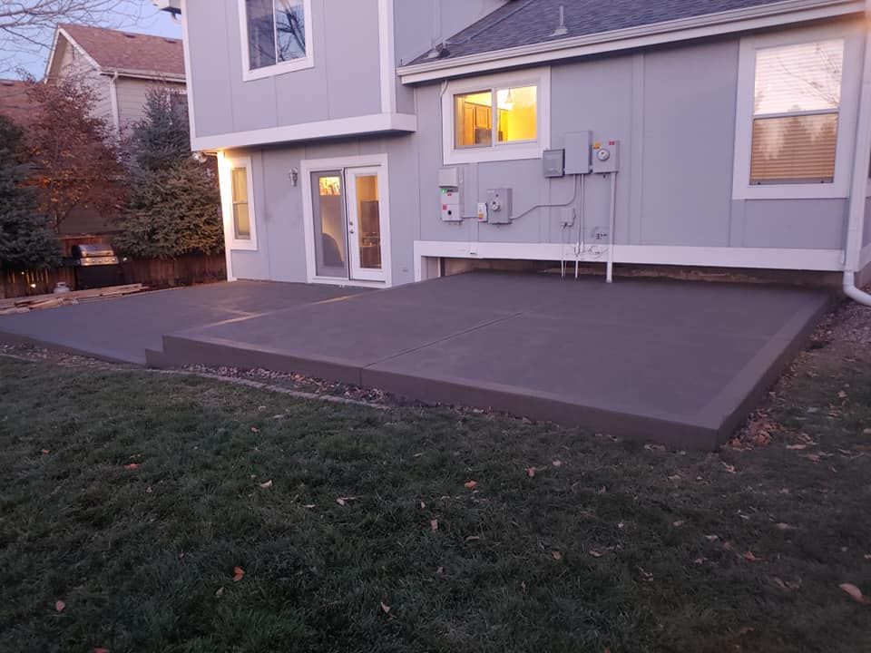 Concrete patio with steps, next to a two-story light blue house with windows and a sliding door.