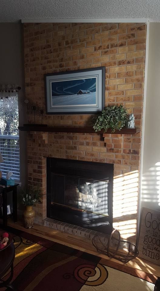 Brick fireplace with a dark wooden mantel, art, and a small plant.