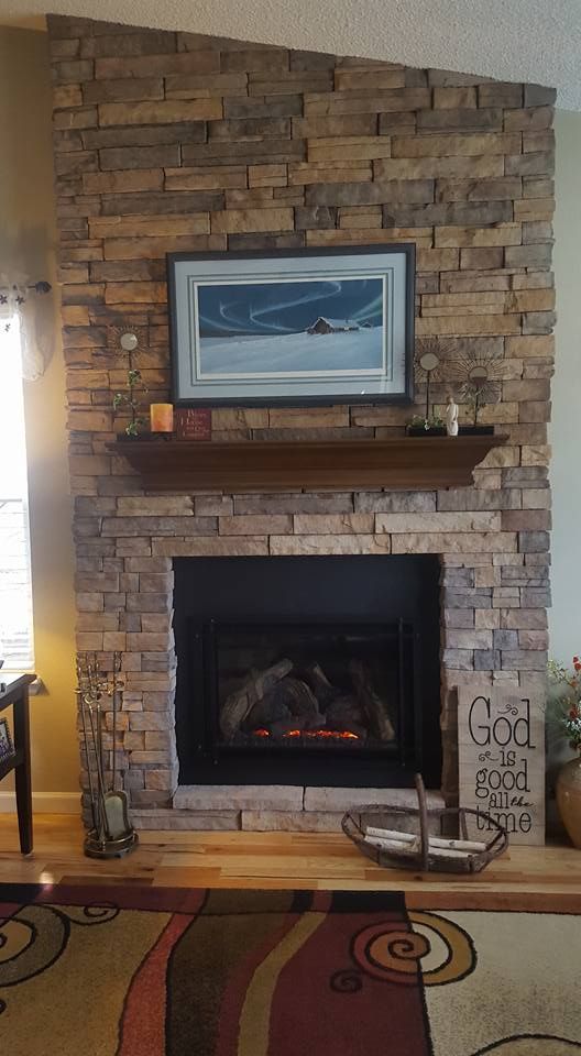 Fireplace with stone facade, dark wooden mantel and art.