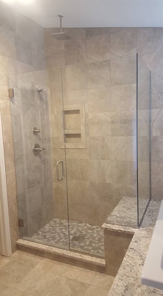 Glass shower enclosure with stone tile walls, pebble floor, and bench.