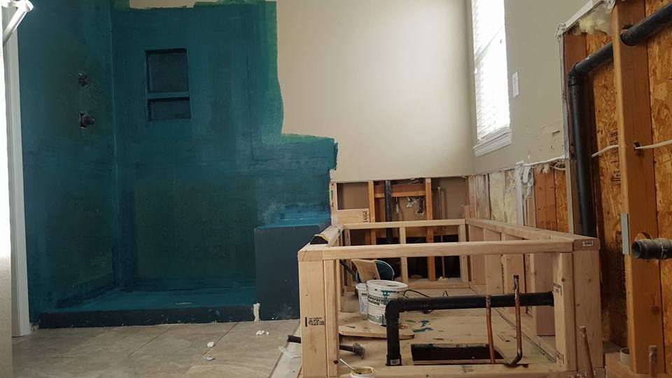 Bathroom renovation: Teal-painted shower walls, exposed framing, damaged drywall, window, and new plumbing.