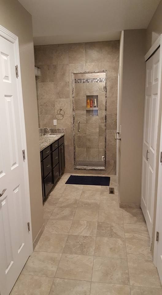 Bathroom with tiled floor and shower, dark cabinets, and white doors.