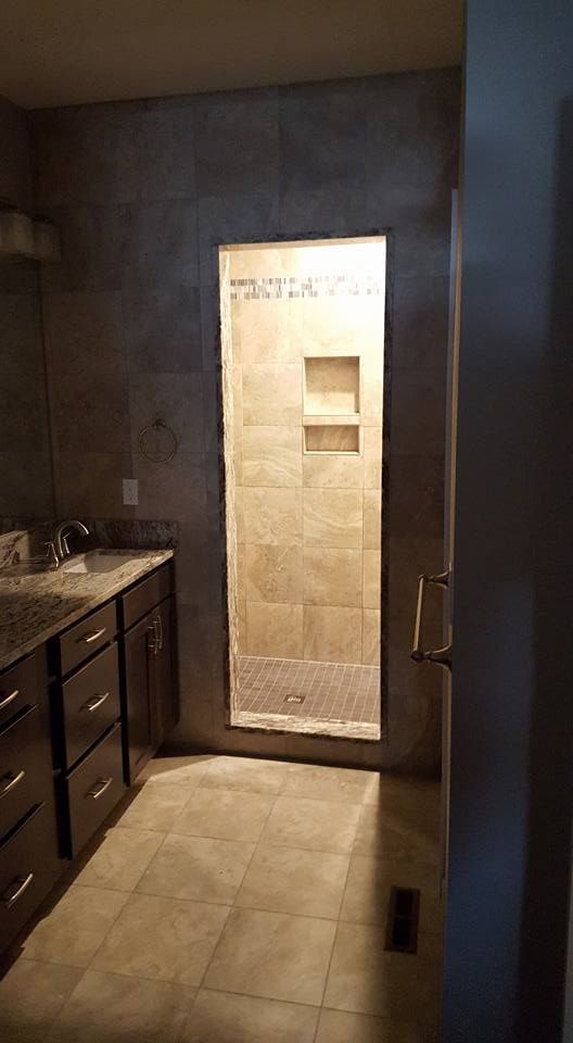 Bathroom with a walk-in shower. Beige and brown tiled surfaces. Dark brown vanity.