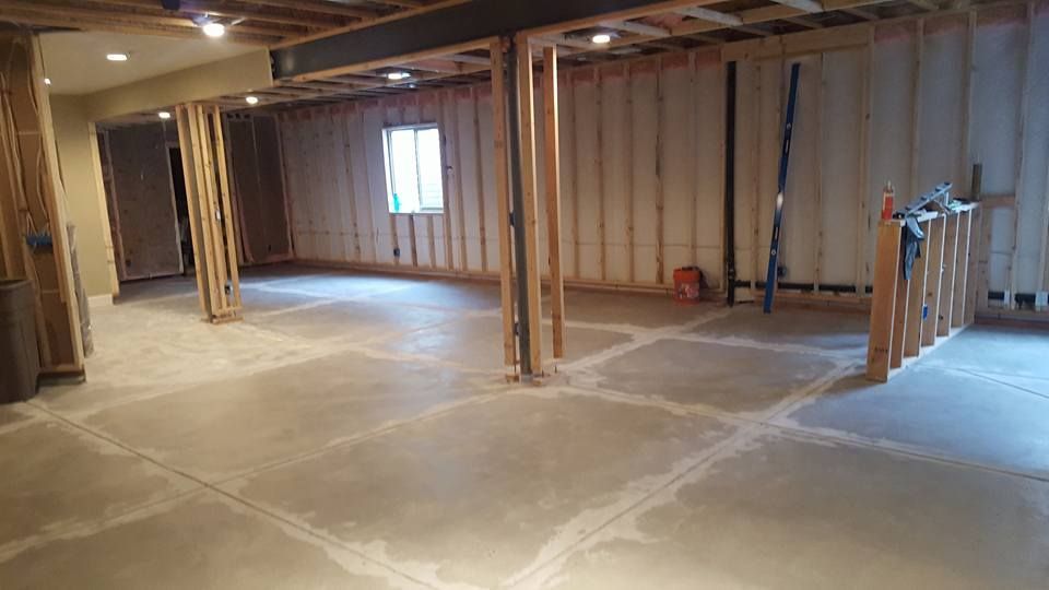 Basement under construction, exposed studs, concrete floor, small window, overhead lights.