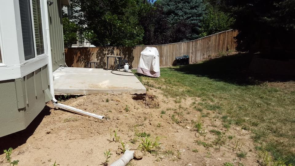 Backyard with a concrete patio, dirt, grass, and a wooden fence.
