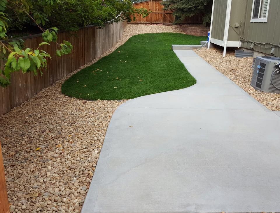 Backyard with concrete path, artificial turf, gravel, and wooden fence.