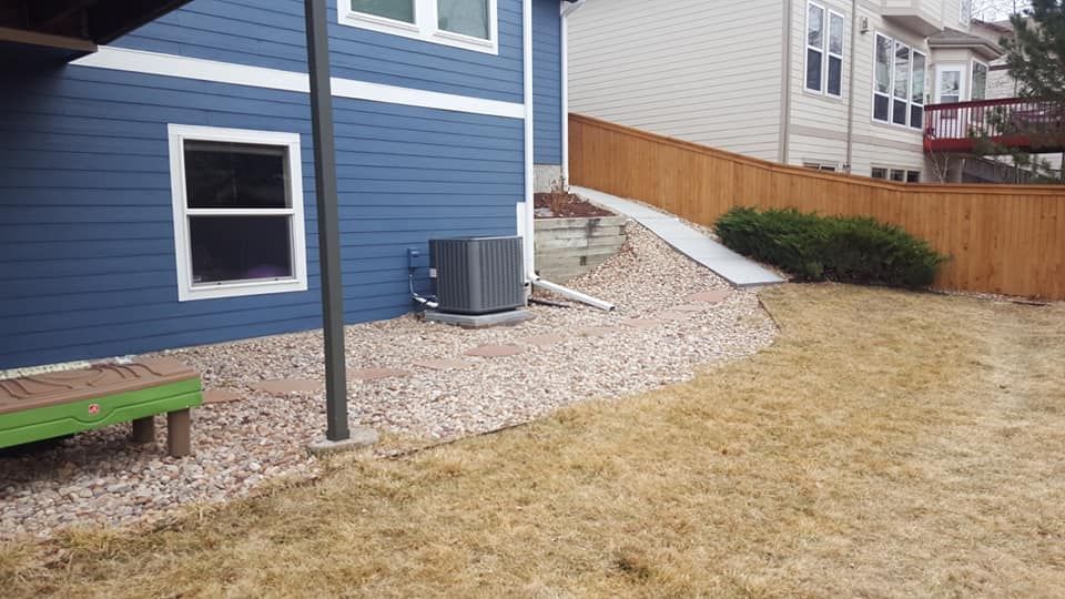 Backyard with a blue house, brown fence, dry grass, and rock landscaping.