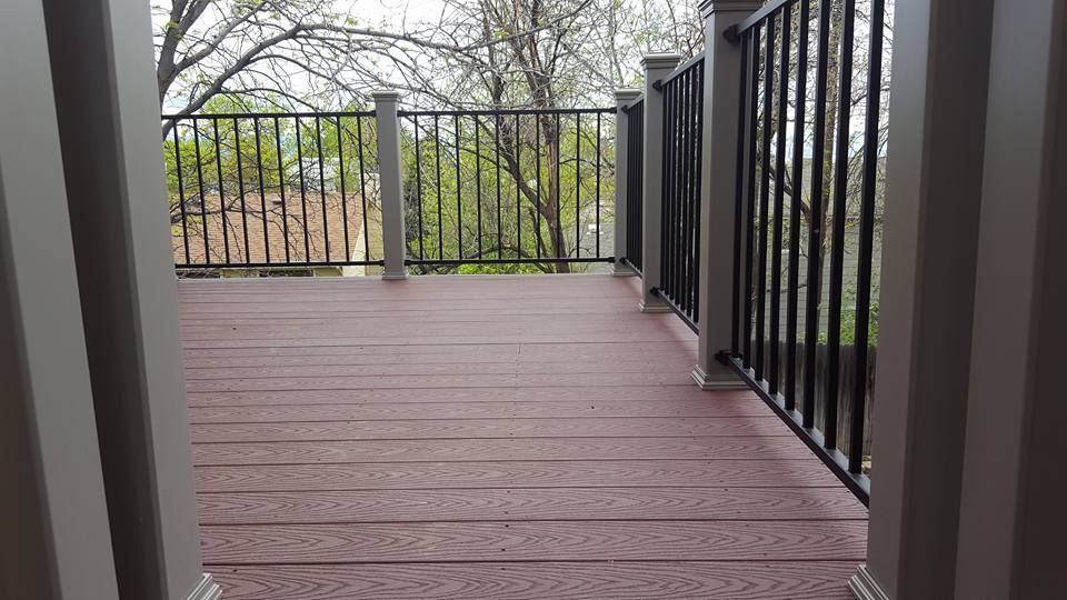 Brown composite deck with black railing overlooking trees.