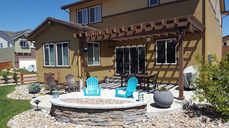Backyard patio with fire pit, pergola, and seating near a two-story house.