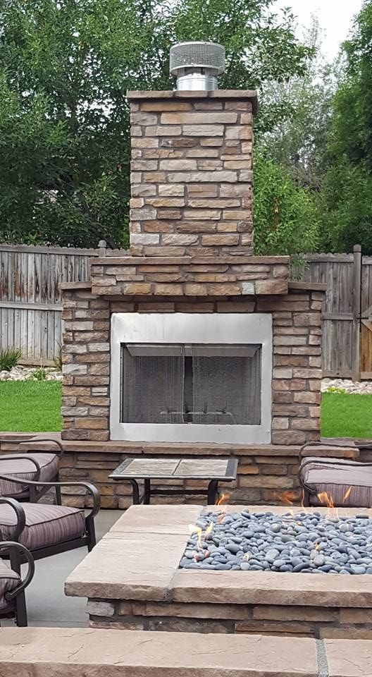 Stone outdoor fireplace with a stainless steel face and chimney.