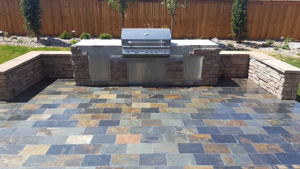 Outdoor kitchen with stone patio, grill, and stone walls.