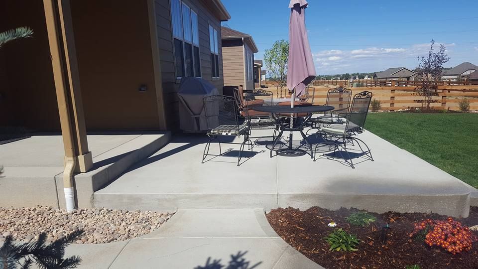 Concrete patio with outdoor table and chairs, near a house with a blue sky.