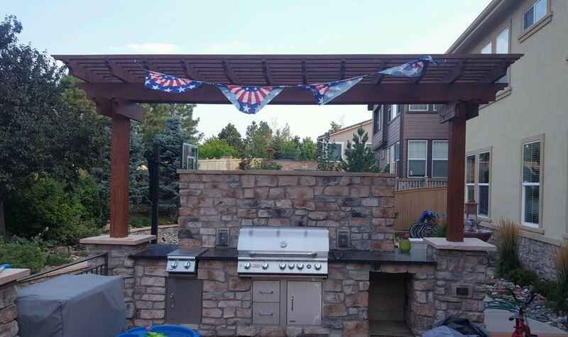 Outdoor kitchen with stone, brown pergola, grill, and decorations.