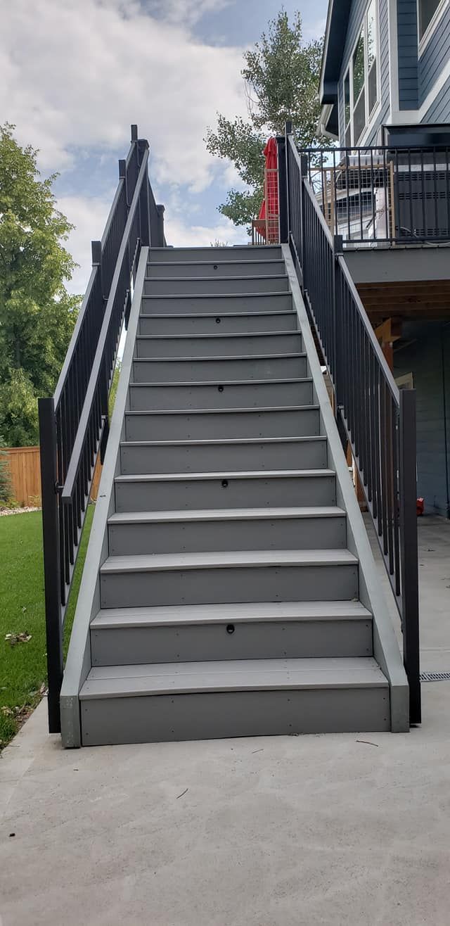 Gray wooden staircase leading up to a deck, with black railings on either side.