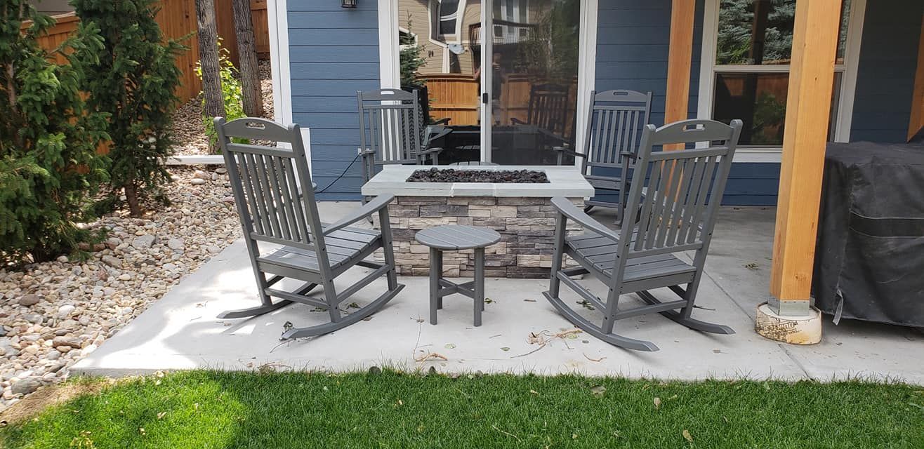 Outdoor patio with gray rocking chairs around a stone fire pit table and small side table.