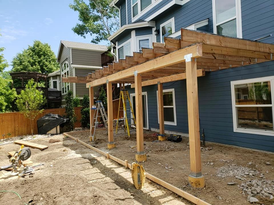 Construction of a wooden pergola attached to a blue house, in a backyard setting.