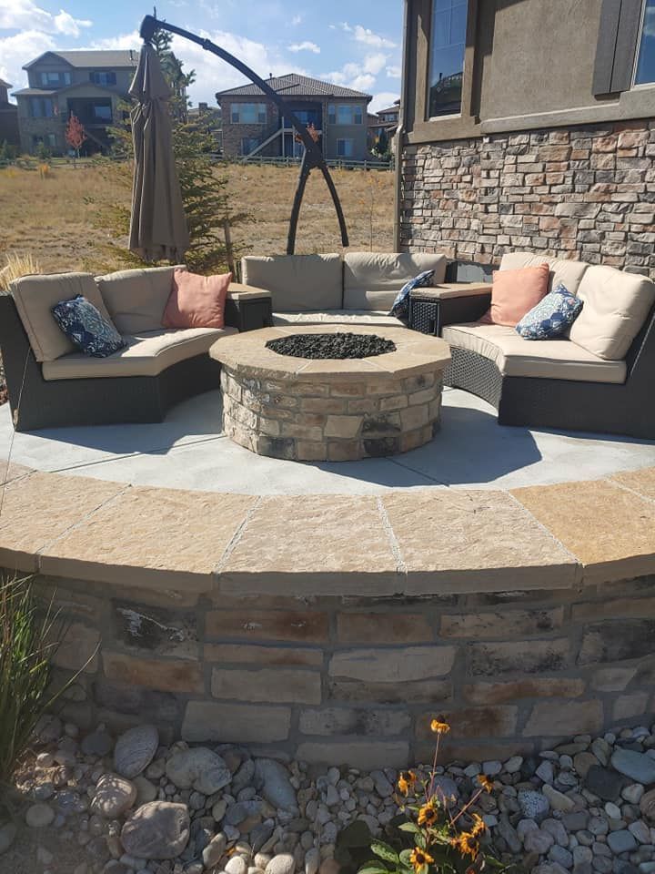 Outdoor patio with a stone fire pit surrounded by wicker furniture and decorative pillows.