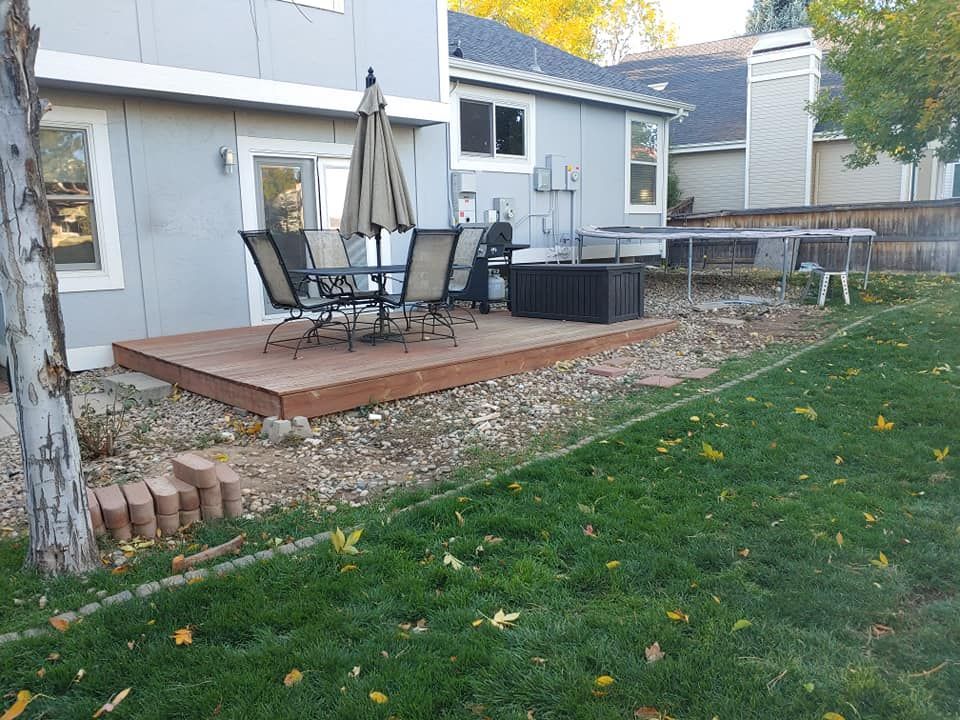 Backyard with deck, patio furniture, fire pit, and trampoline near a house with gray siding and green grass.