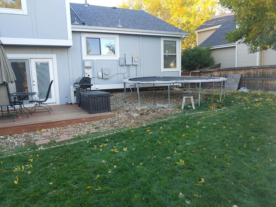 Backyard with light blue house, trampoline, patio, and green grass.