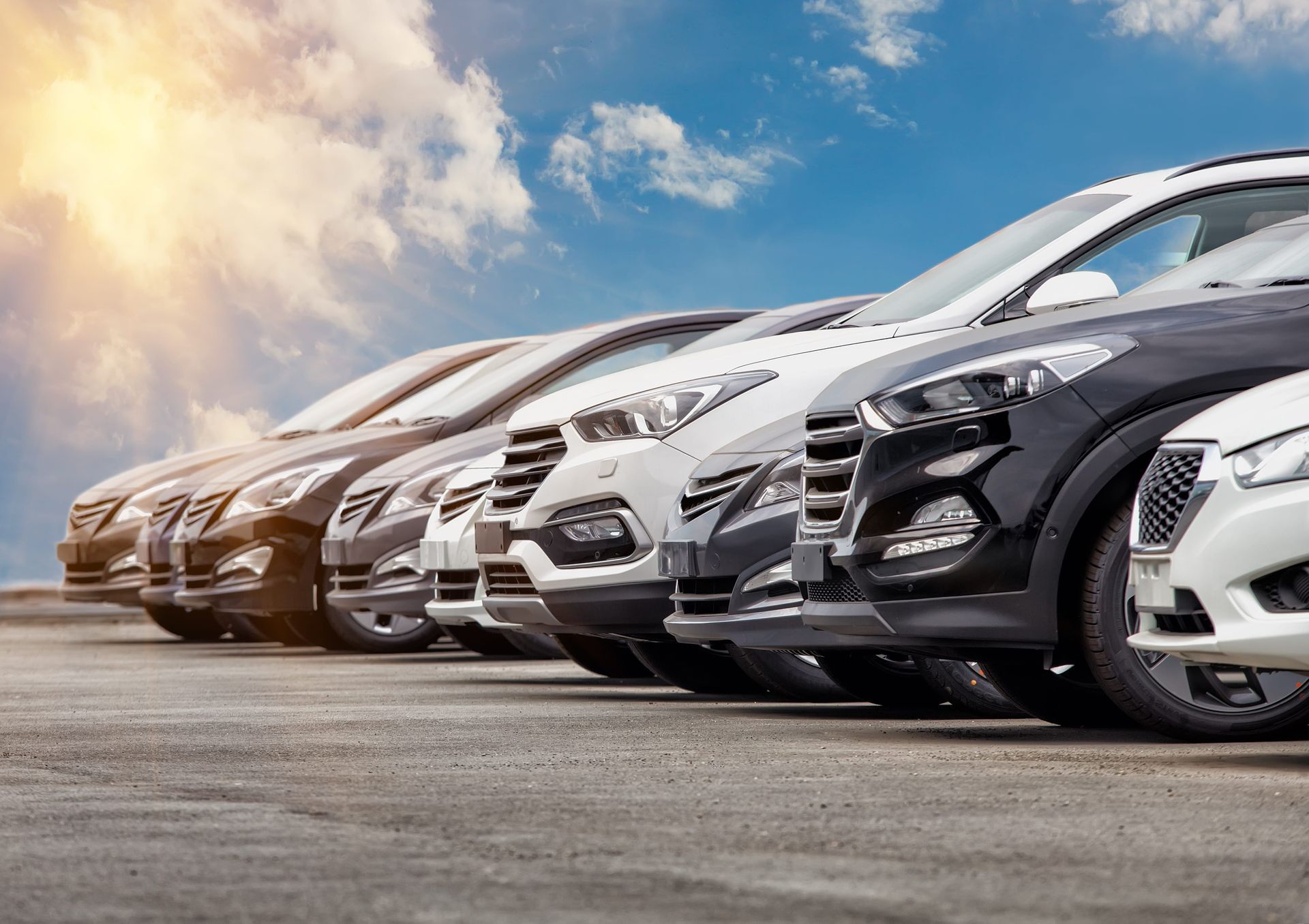 Row of parked cars lined up in a dealership lot under a cloudy sky