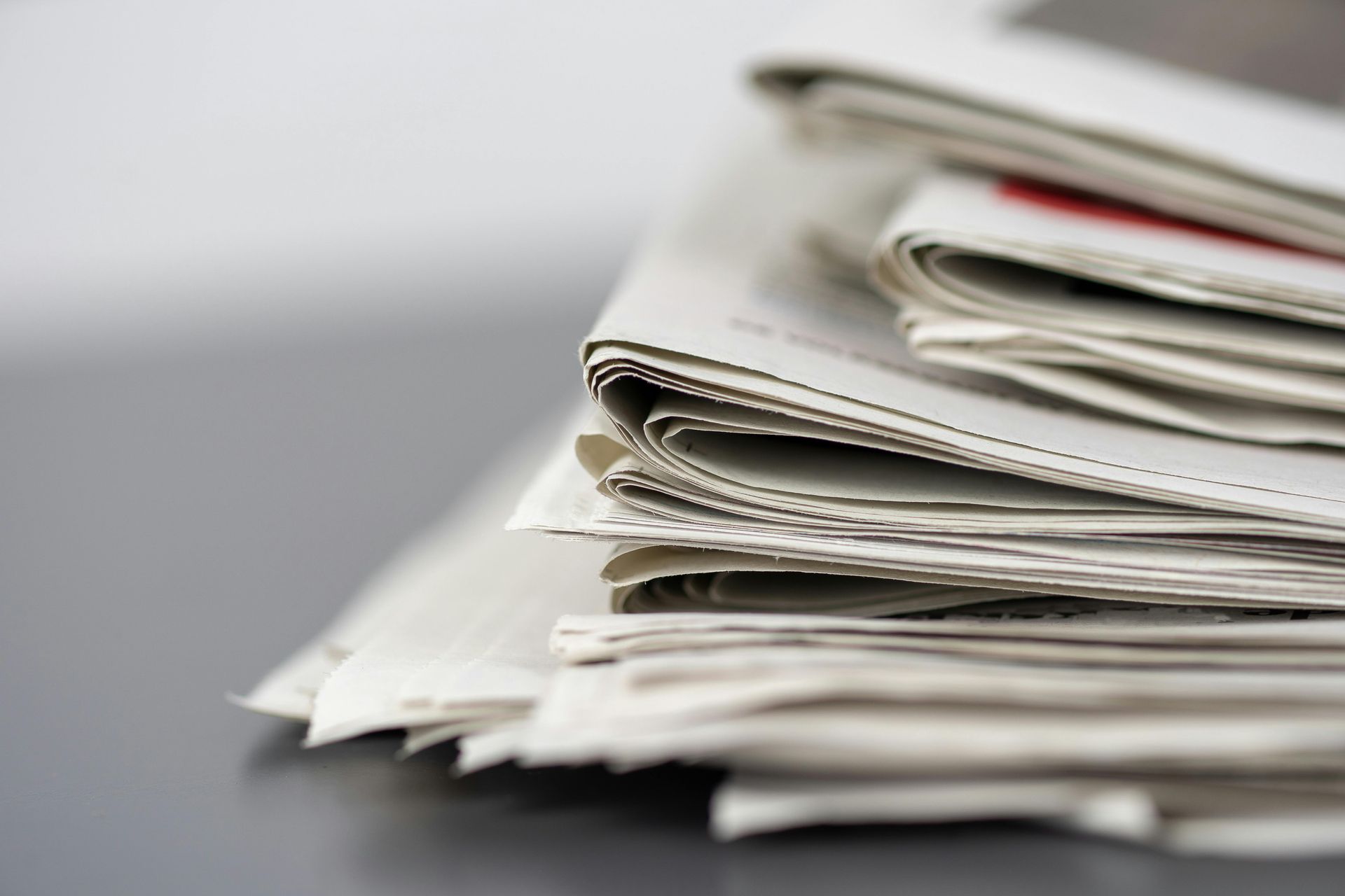 A stack of folded newspapers resting on a flat, dark surface, captured from a side angle.
