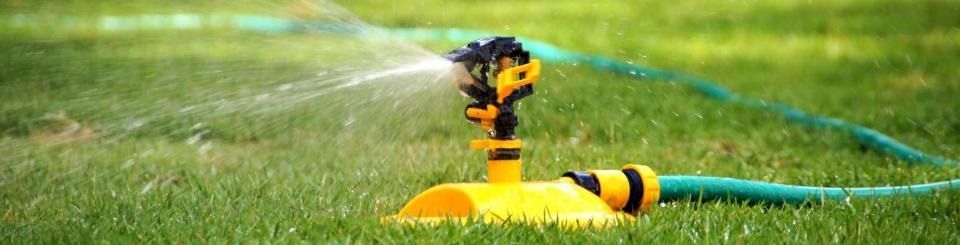 Yellow sprinkler spraying water on a green lawn with a blue hose attached