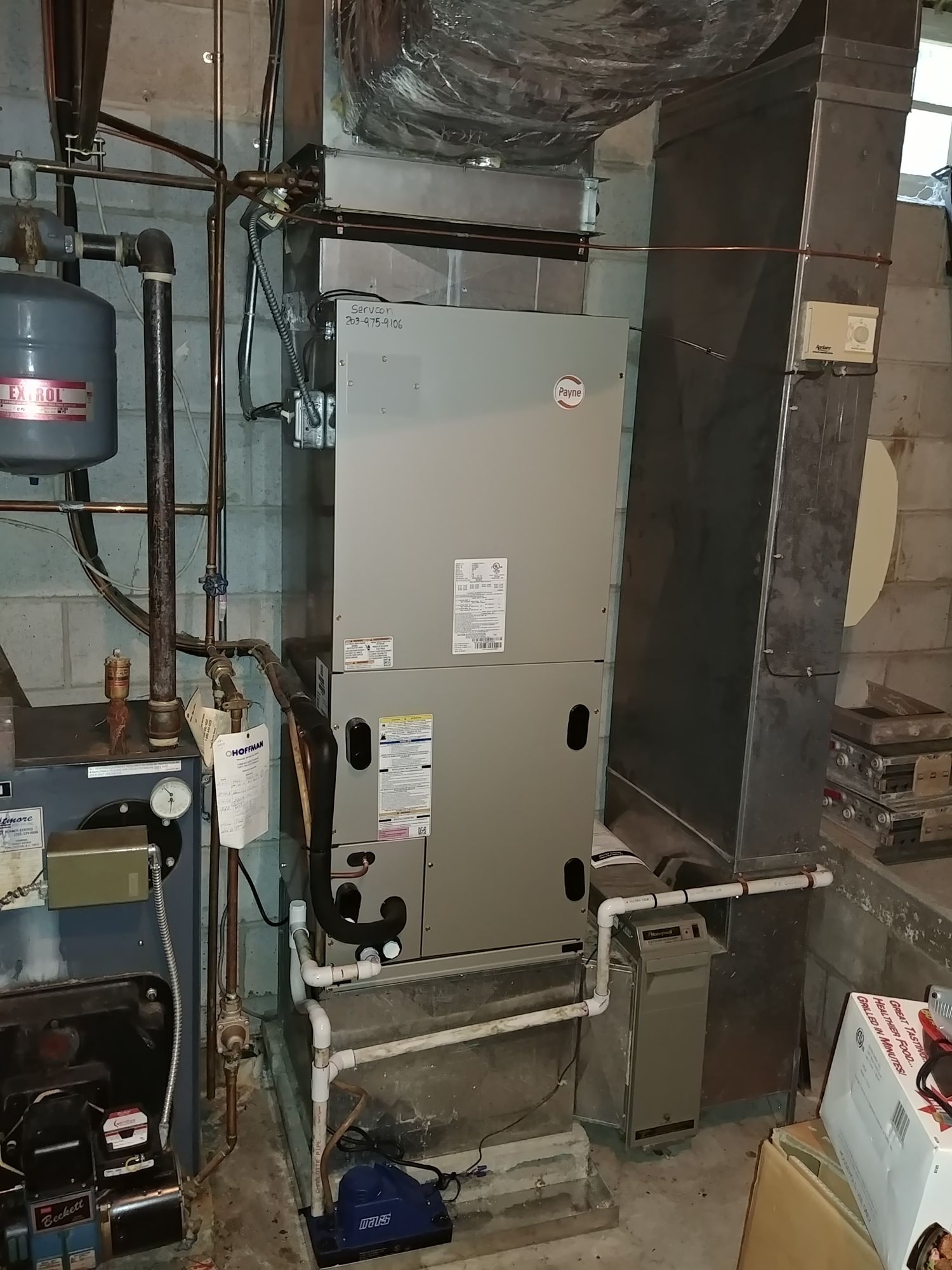 A furnace is sitting in a basement next to a water heater.
