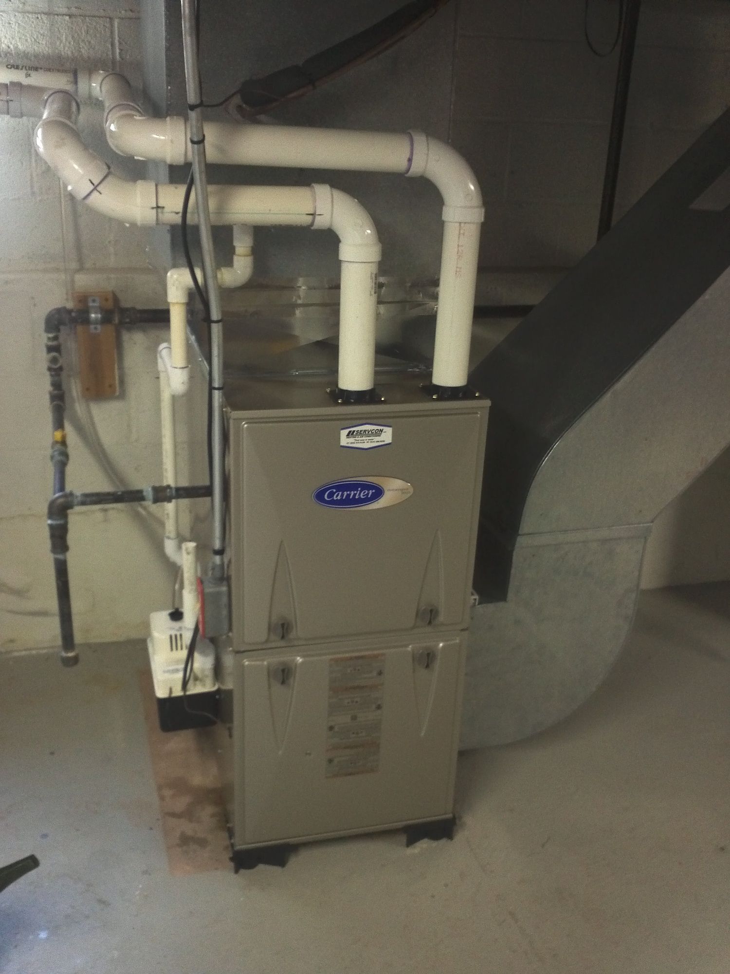 A furnace is sitting in a basement next to a staircase.