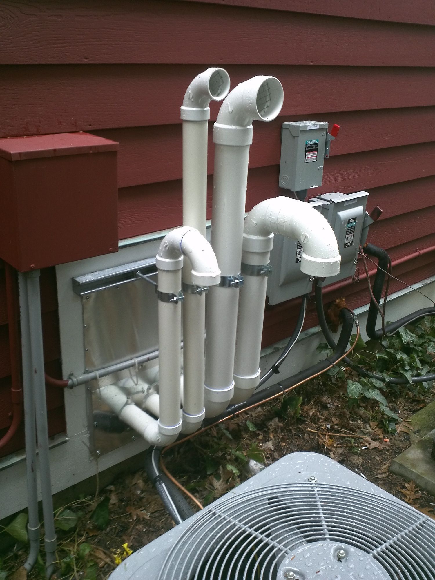A gray air conditioner is sitting on the side of a red house.