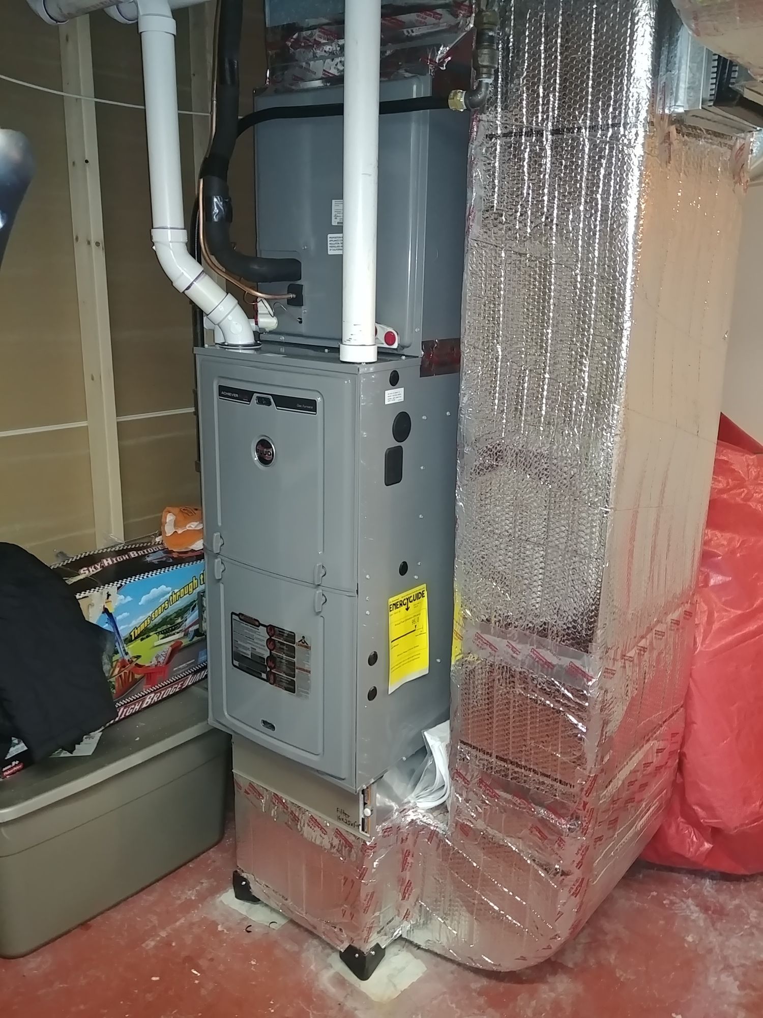 A furnace is sitting in a basement next to a duct.