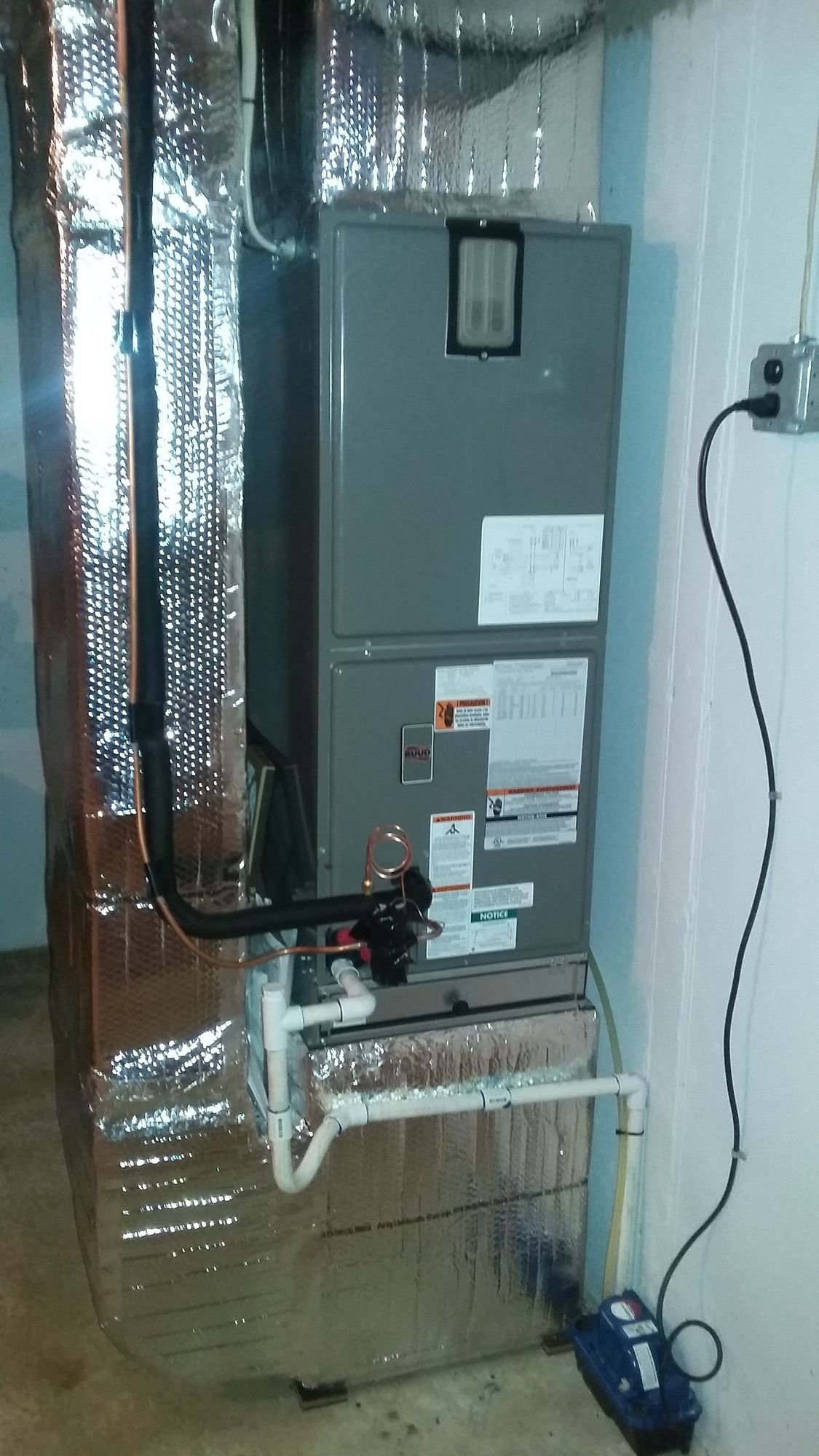 A furnace is sitting in a basement next to a wall.