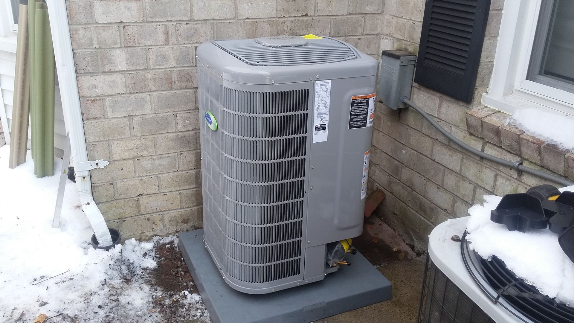 A gray air conditioner is sitting outside of a brick building.