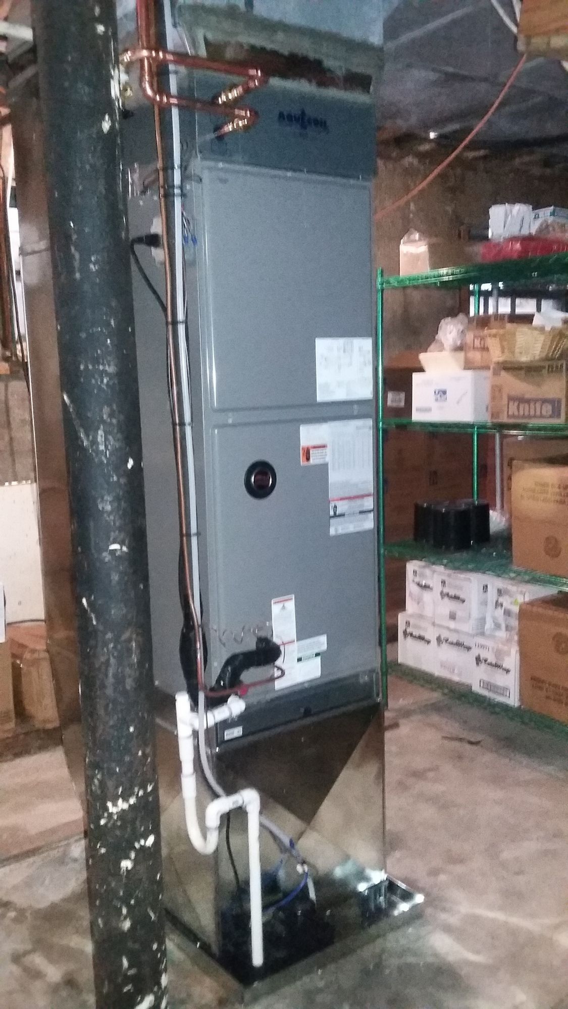 An air conditioner is sitting in a basement next to a pipe.