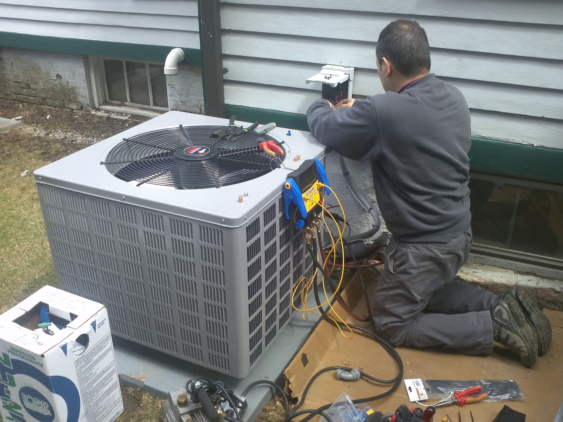 A man is working on an air conditioner outside of a house.