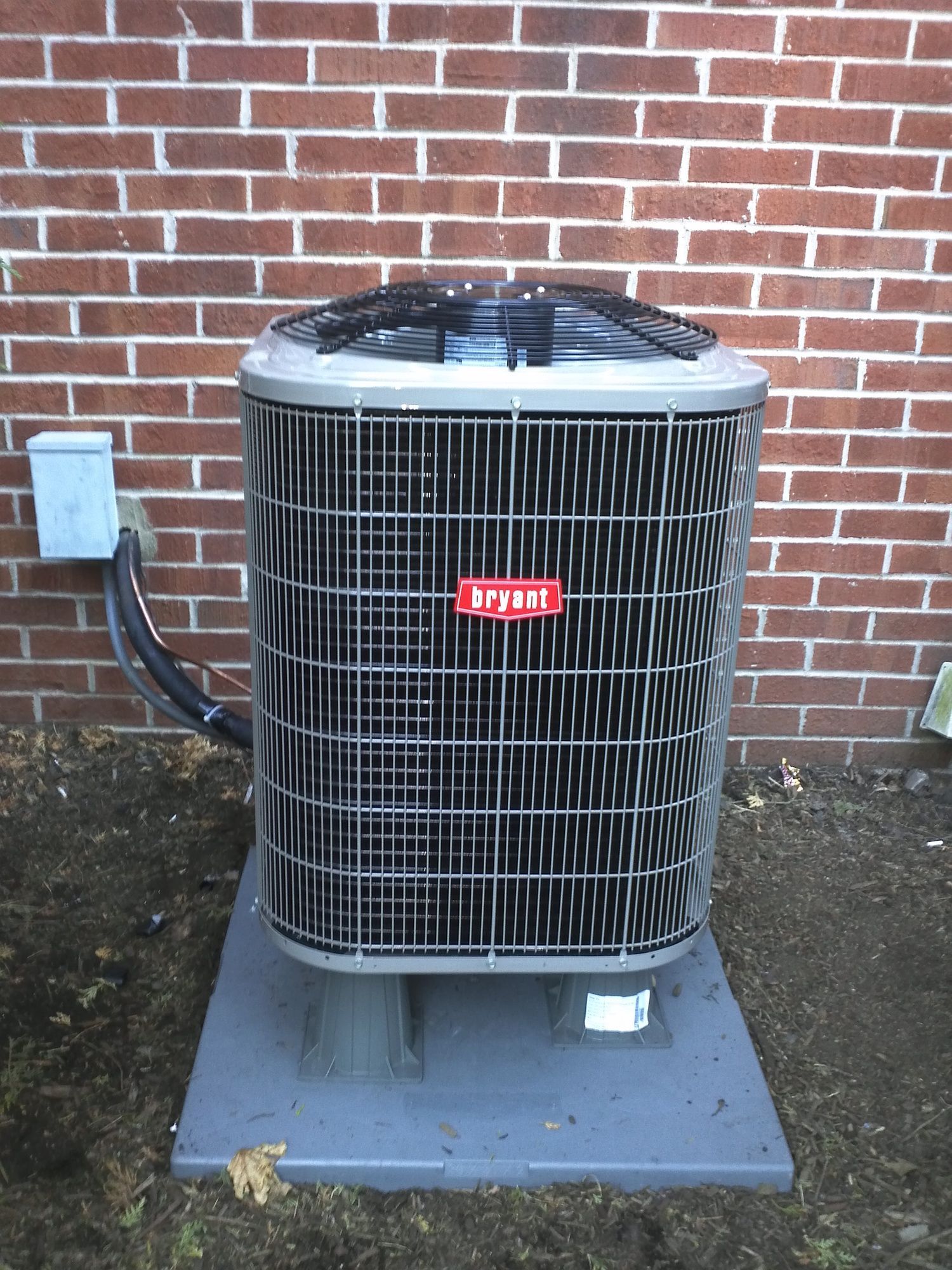 A bryant air conditioner is sitting in front of a brick wall