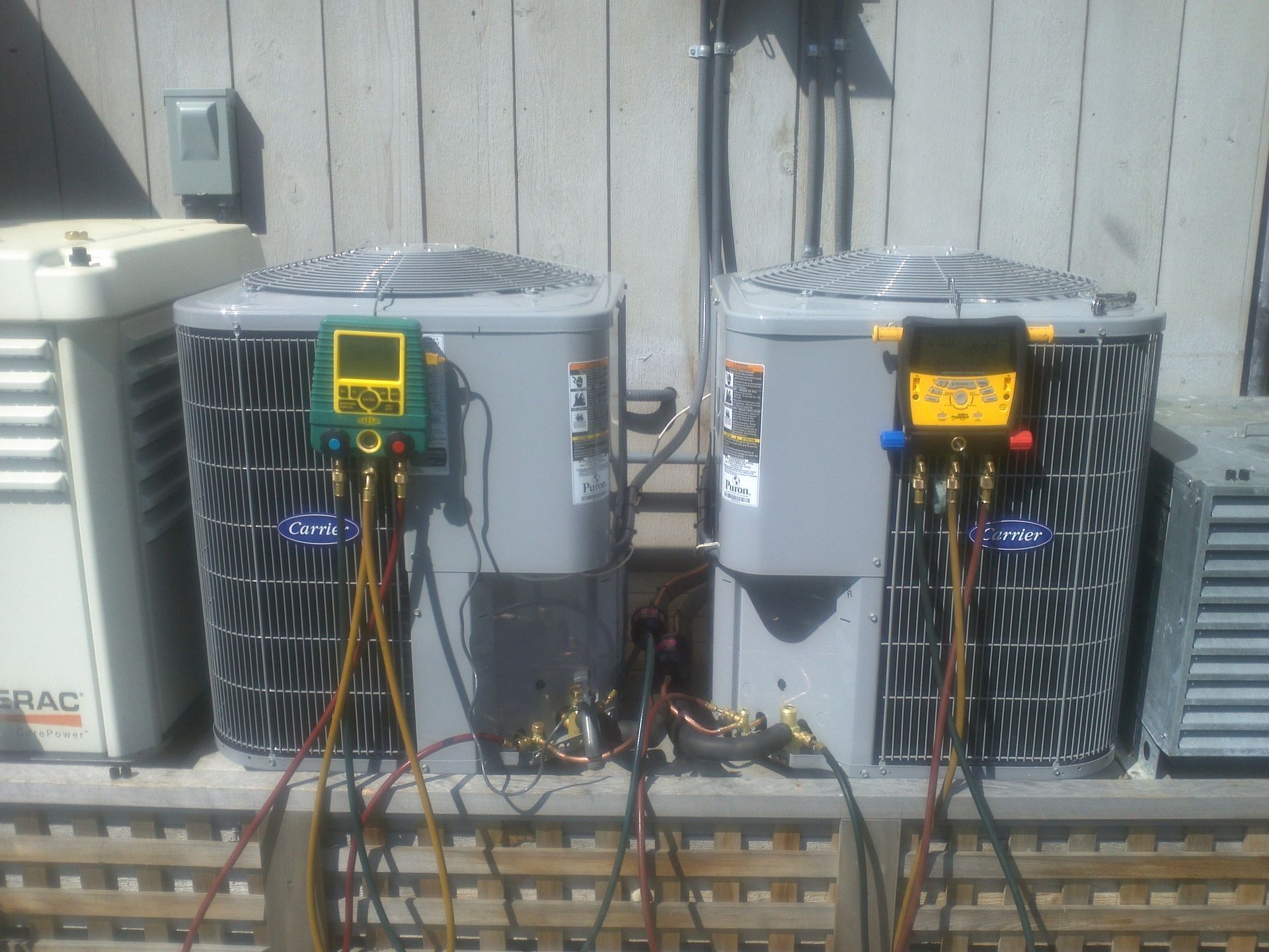 Two air conditioners are sitting next to each other on a wooden fence.