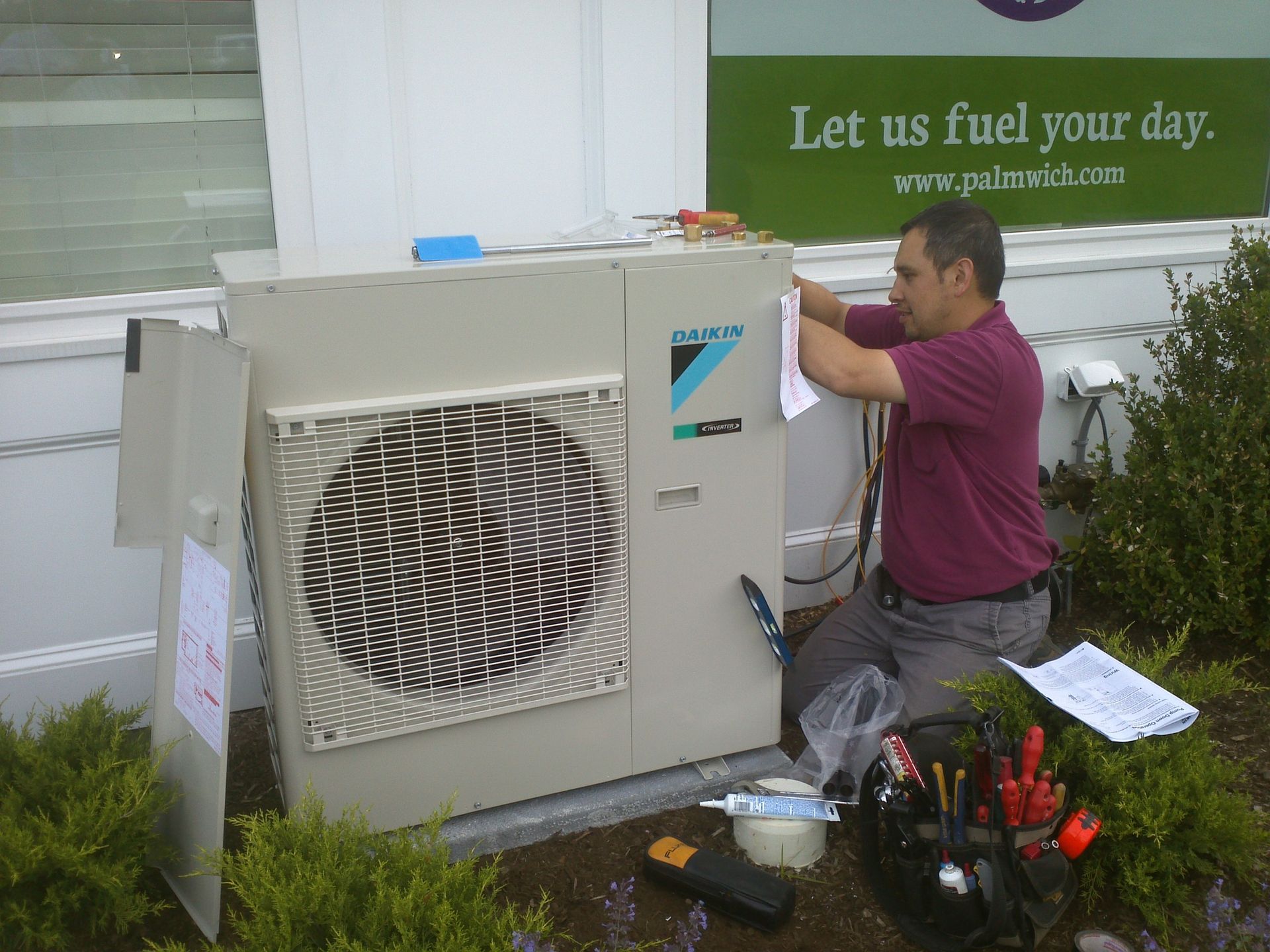 A man is working on an air conditioner in front of a sign that says let us fuel your day