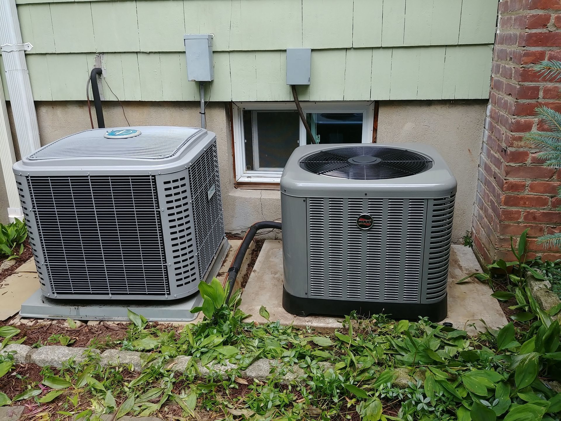 Two air conditioners are sitting outside of a house.