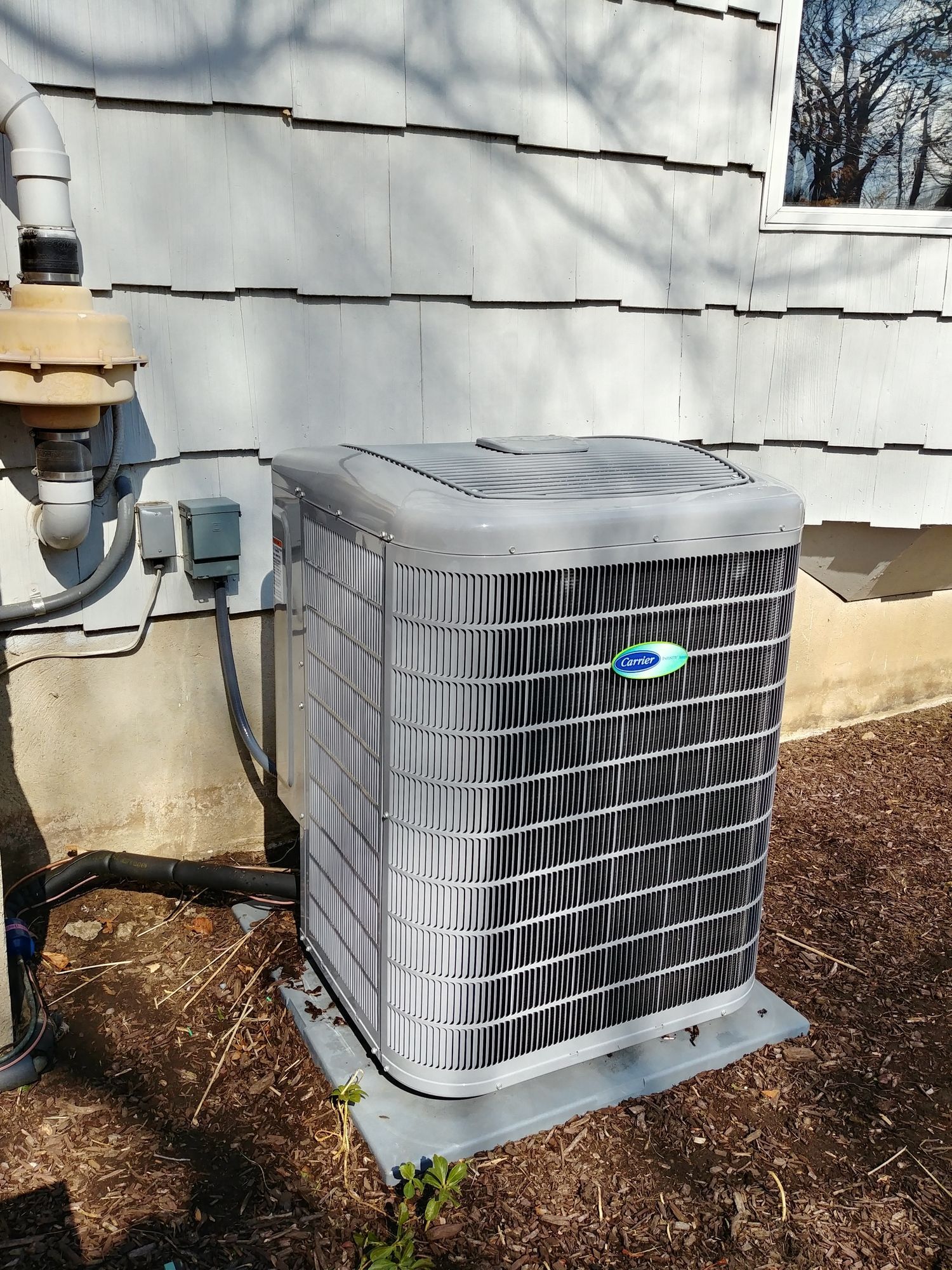 An air conditioner is sitting outside of a house next to a window.
