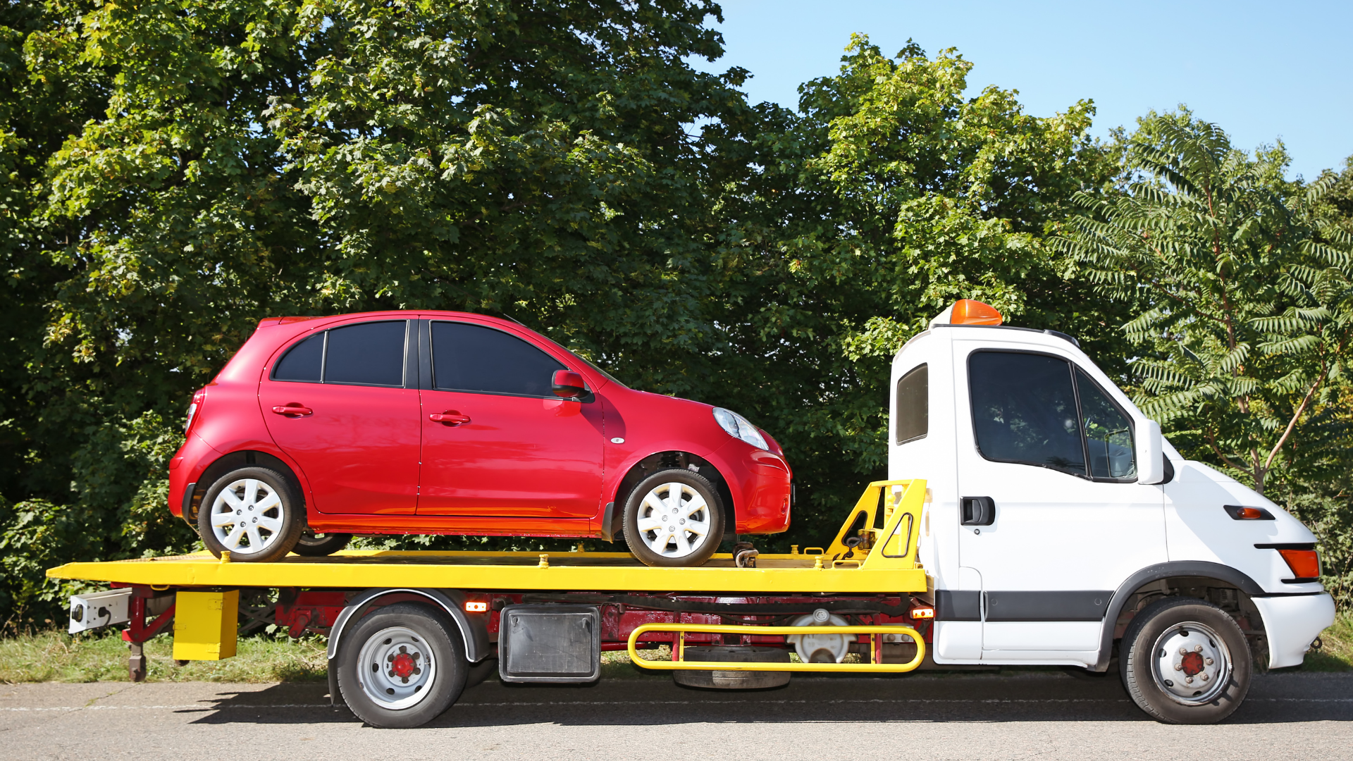 Tow truck towing a black SUV on a dark road at sunset.