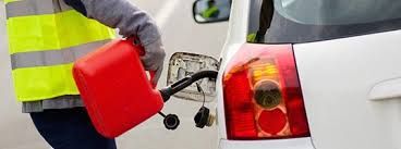 Fuel truck being unloaded at a gas station, worker in safety vest connecting a hose to the truck.