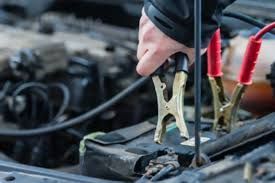 A person connecting a car battery charger to a car battery in an engine bay.